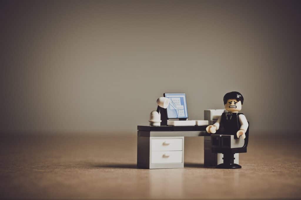 Busy work concept: a toy sales rep sitting at a desk is isolated and stressed.