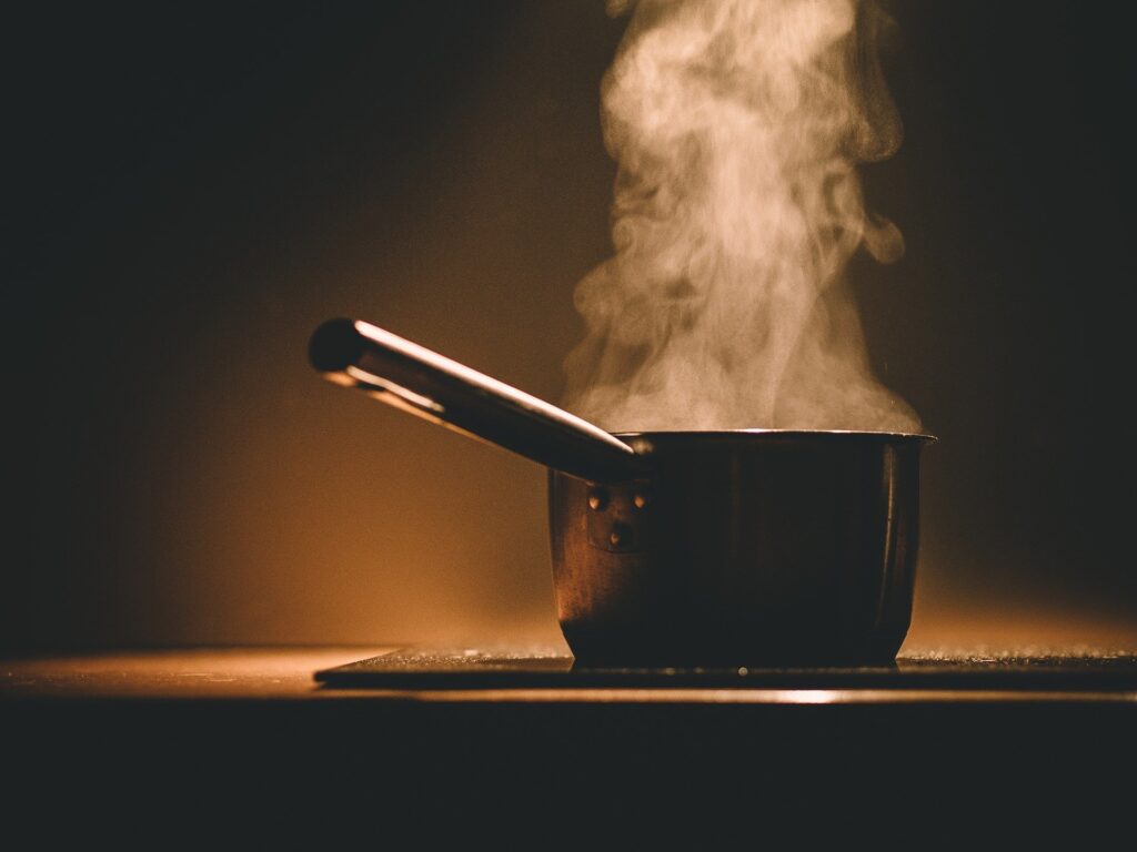 Content approval concept: a boiling pot rests on a stove eye under a dim light.