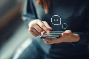 A woman holds and taps on a smartphone screen as two live-chat bubbles with ellipses hover over it.