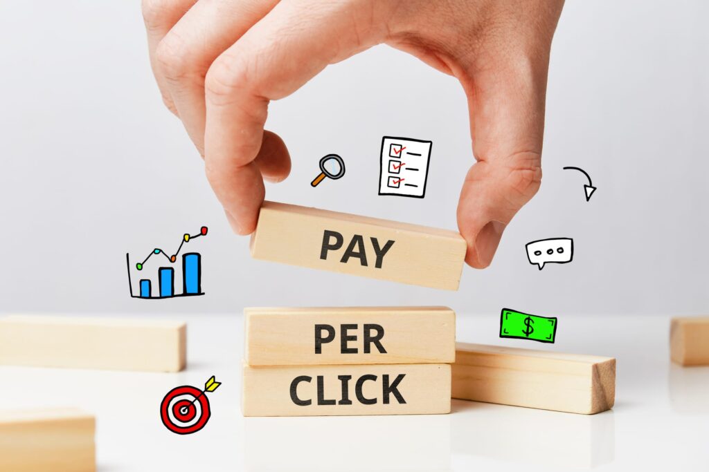 PPC concept: "pay-per-click" spelled out with individual words printed on building blocks, set on a table around icons for revenue, sales growth, lead targeting, checklists, and more.