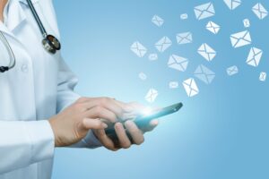 Email list health concept: email icons fly from a smartphone held by a doctor wearing a white coat and stethoscope.