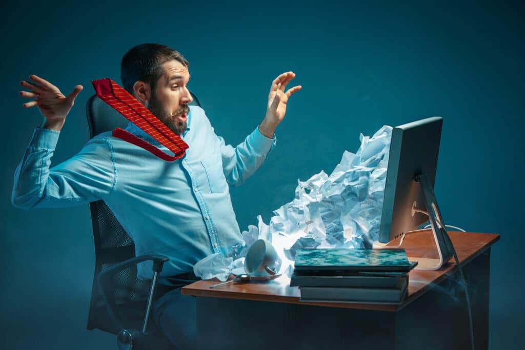 Prospecting emails concept: a business rep reels back as crumpled paper pours from his computer screen onto his desk.