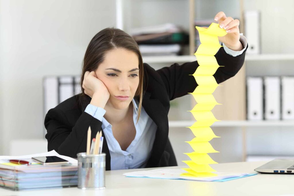 A burned out sales rep plays with a ream of yellow Post-it notes on her desk.