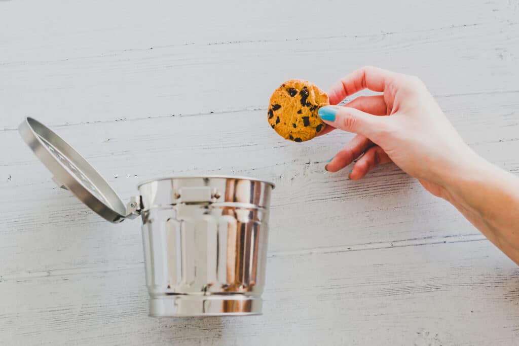 A hand tosses a cookie into a small metal trashcan.