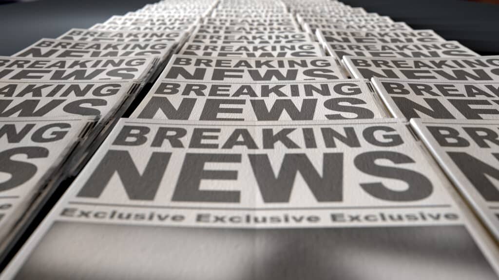 A long row of folded newspapers at the end of a press run with a generic headline that reads "Breaking News" on the front page on an isolated white background.