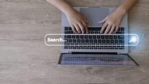 Long-tail keyword concept: an overhead view of hands typing on a laptop while a search bar is superimposed over the keyboard.