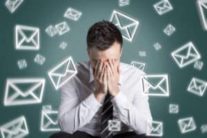 A marketer hangs his head in his hands while email icons swarm around him.