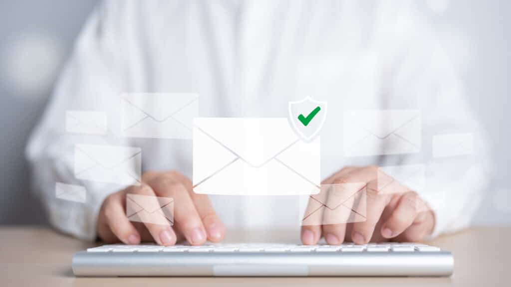 DMARC concept: an email icon with a green checkmark hovers over the hands of a marketing lead who is typing on a keyboard. This represents successful email authentication.