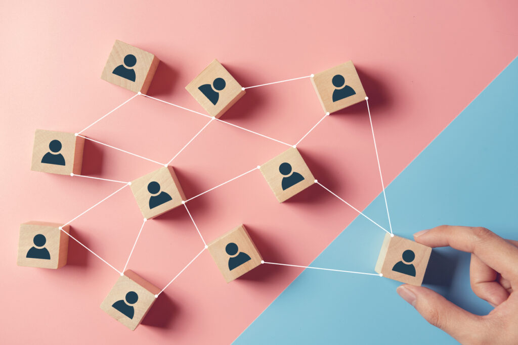 Segment your emails concept: a wooden block with a person icon is moved by hand from a group of other blocks on a pink background to one that is blue.
