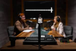 A smartphone records two marketers in a podcast booth.